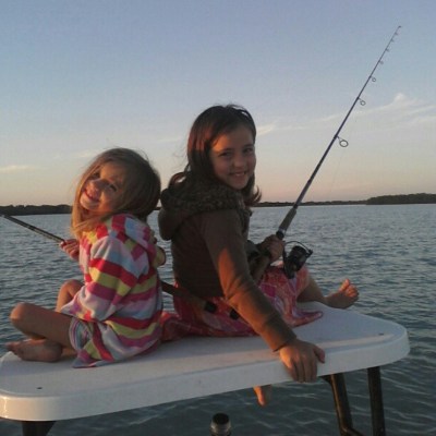 Two smiling children fishing on a boat during sunset.