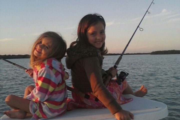 Two smiling children fishing on a boat during sunset.