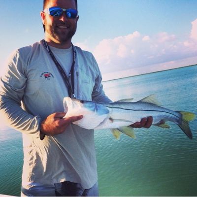 Man holding a fish on a boat with blue water and cloudy sky in the background.