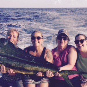 Four people on a boat holding a large fish with the ocean in the background.