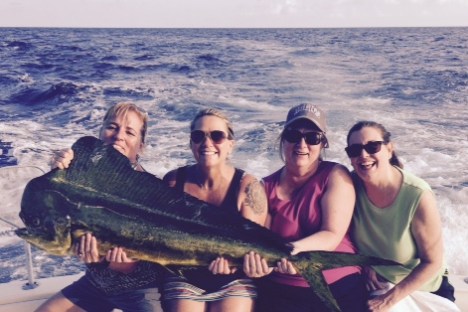 Four people on a boat holding a large fish with the ocean in the background.