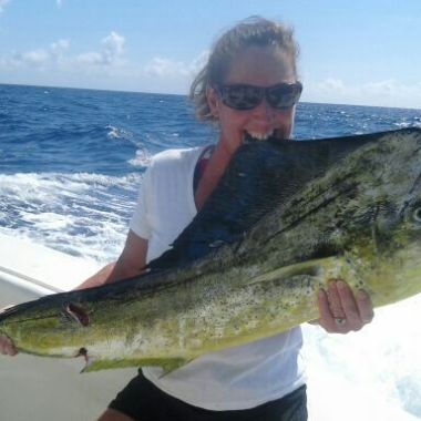 Person holding a large fish on a boat with an ocean background.