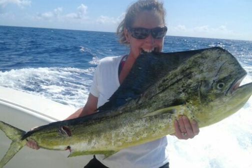 Person holding a large fish on a boat with an ocean background.