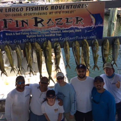 Seven people in front of hanging fish with a Key Largo fishing sign above.