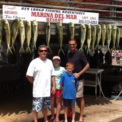 Group of people posing under a sign with hanging fish at a marina.