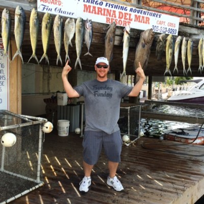Person posing with a line of hanging fish on a dock near the Marina Del Mar sign.