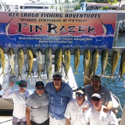 Group of people posing under a fishing sign with a row of fish displayed.