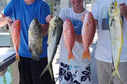 Three men in sunglasses holding five caught fish on a dock.