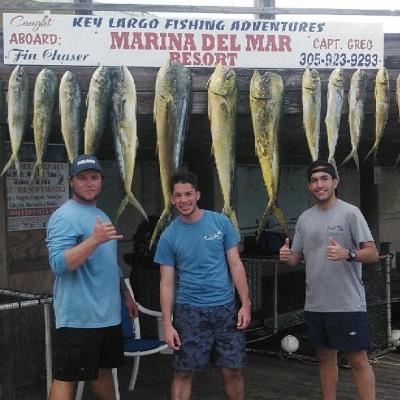 Three men posing with a row of large fish hanging on display at a marina fishing resort.