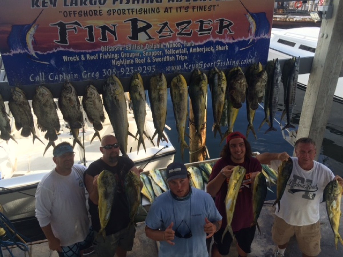 Five people stand holding large freshly caught fish under a sign for Fin Razer sportfishing.
