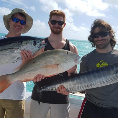 Three men on a boat holding large fish against a turquoise sea horizon.