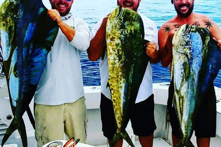Three men on a boat holding large fish, smiling at the camera.
