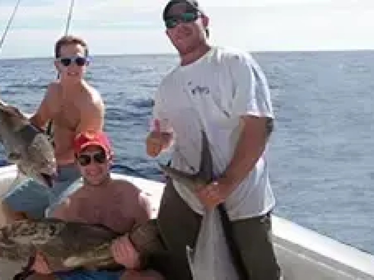 Four people on a boat holding large fish, smiling, and posing for a photo.