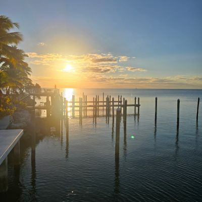 Sunset over a calm sea with a wooden pier and palm trees.