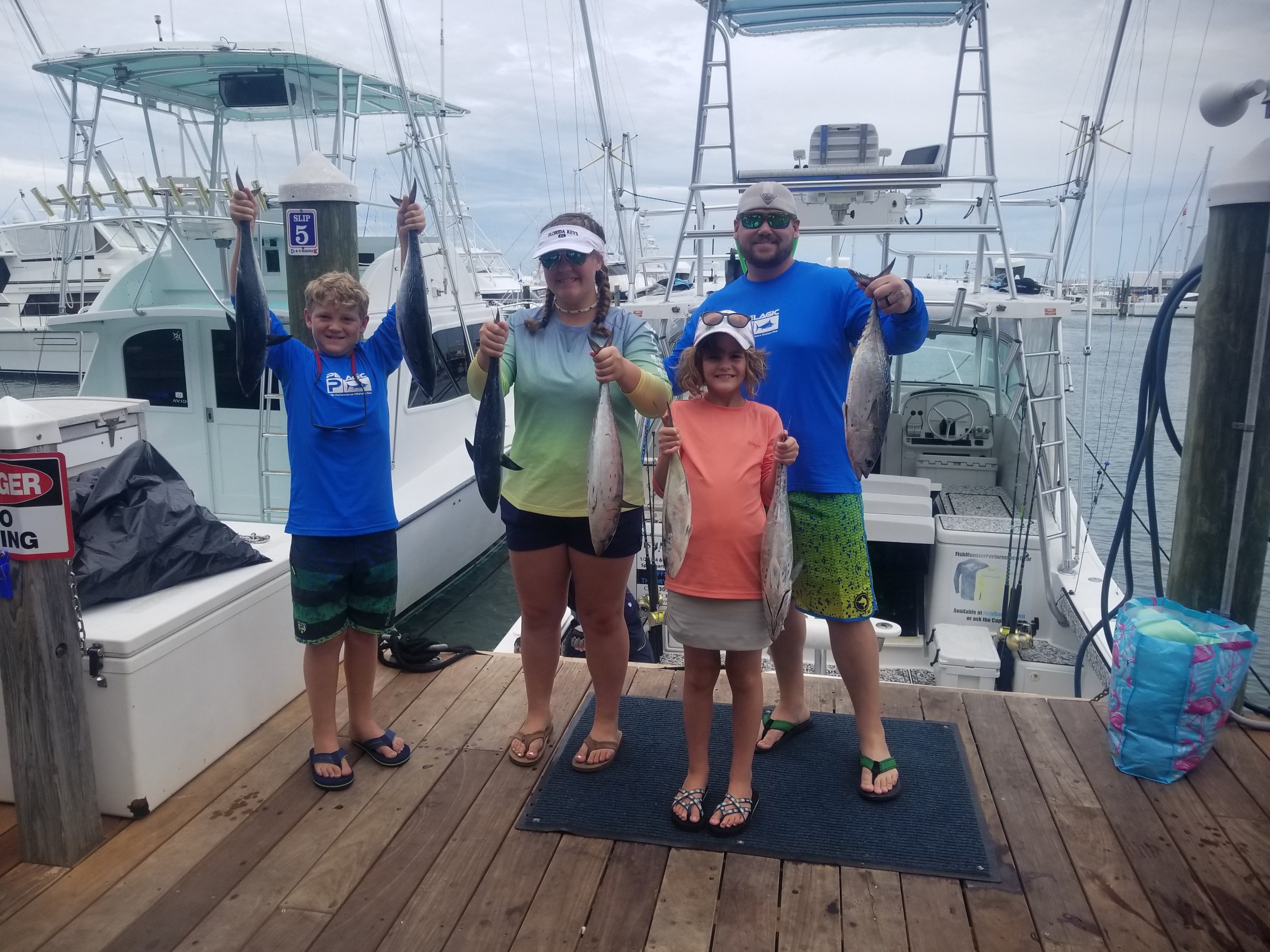 Four people holding fish on a dock with boats in the background.
