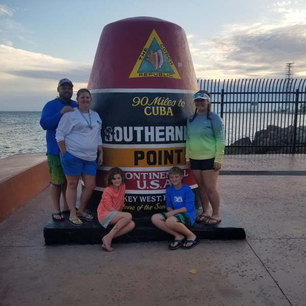 Group posing by Southernmost Point Buoy in Key West at sunset.