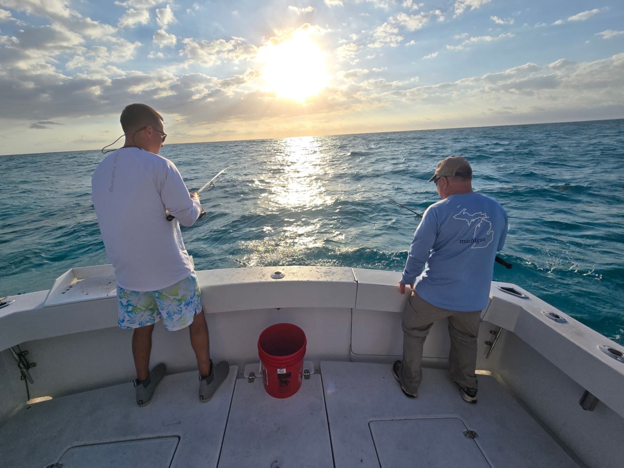 Two people fishing on a boat at sunset with ocean in the background.