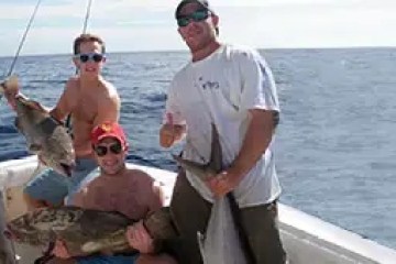 Four people on a boat holding large fish with ocean in the background.