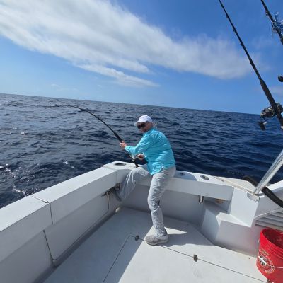 Person fishing on a boat in the ocean under a clear blue sky.