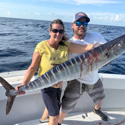 Two people on a boat holding a large fish with the ocean in the background.