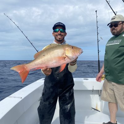 Man holding a large fish on a boat, wearing sunglasses and a hat.