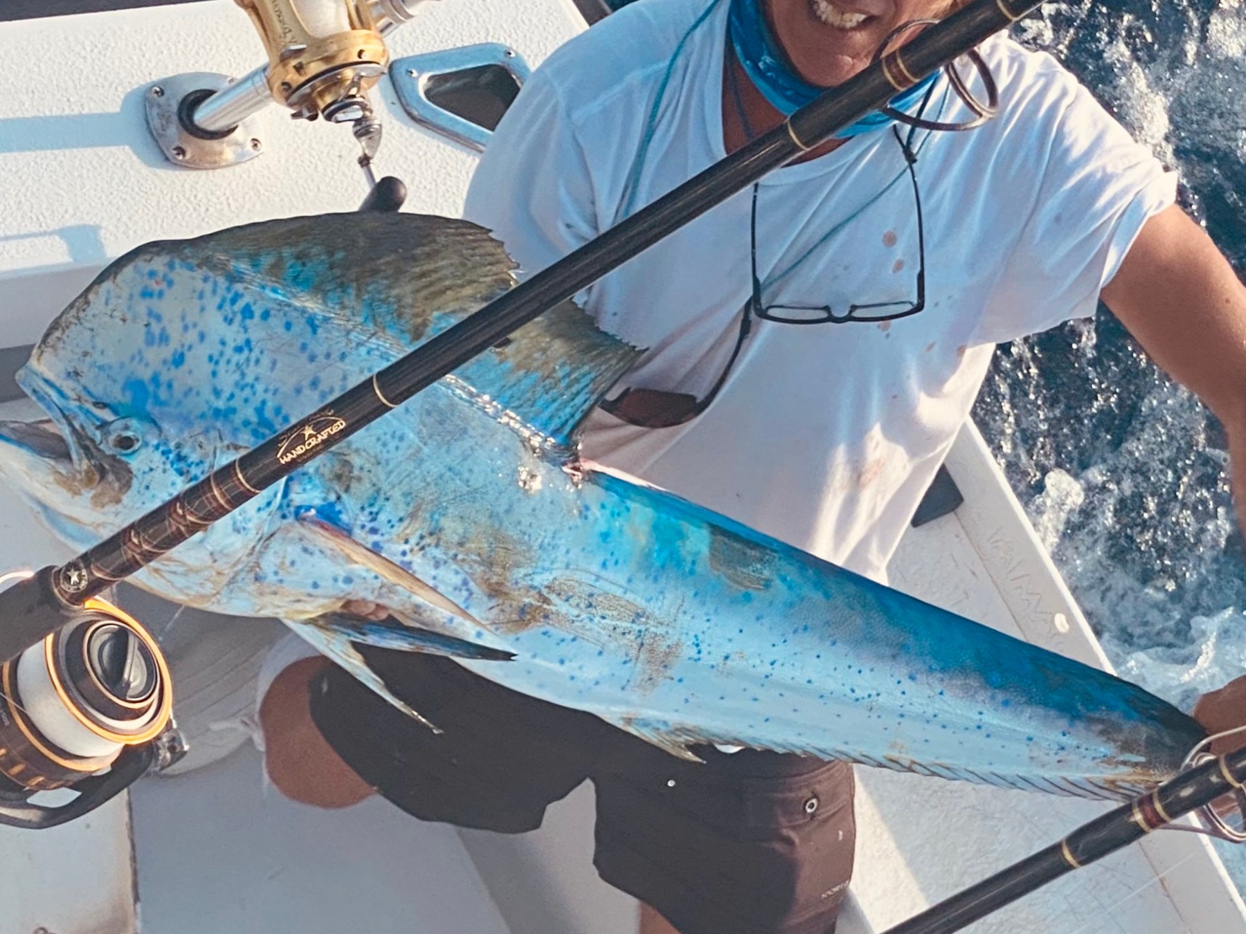 Person on boat holding a large blue fish and fishing rod, with ocean background.