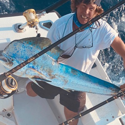 Person on boat holding a large blue fish and fishing rod, with ocean background.