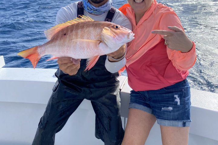 Two people on a boat holding a fish, with the ocean as the background.