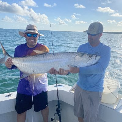 Two people on a boat holding a large fish, with ocean and blue sky in background.