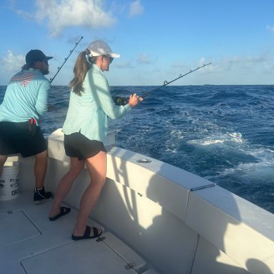 Two people fishing on a boat in the ocean under a blue sky.