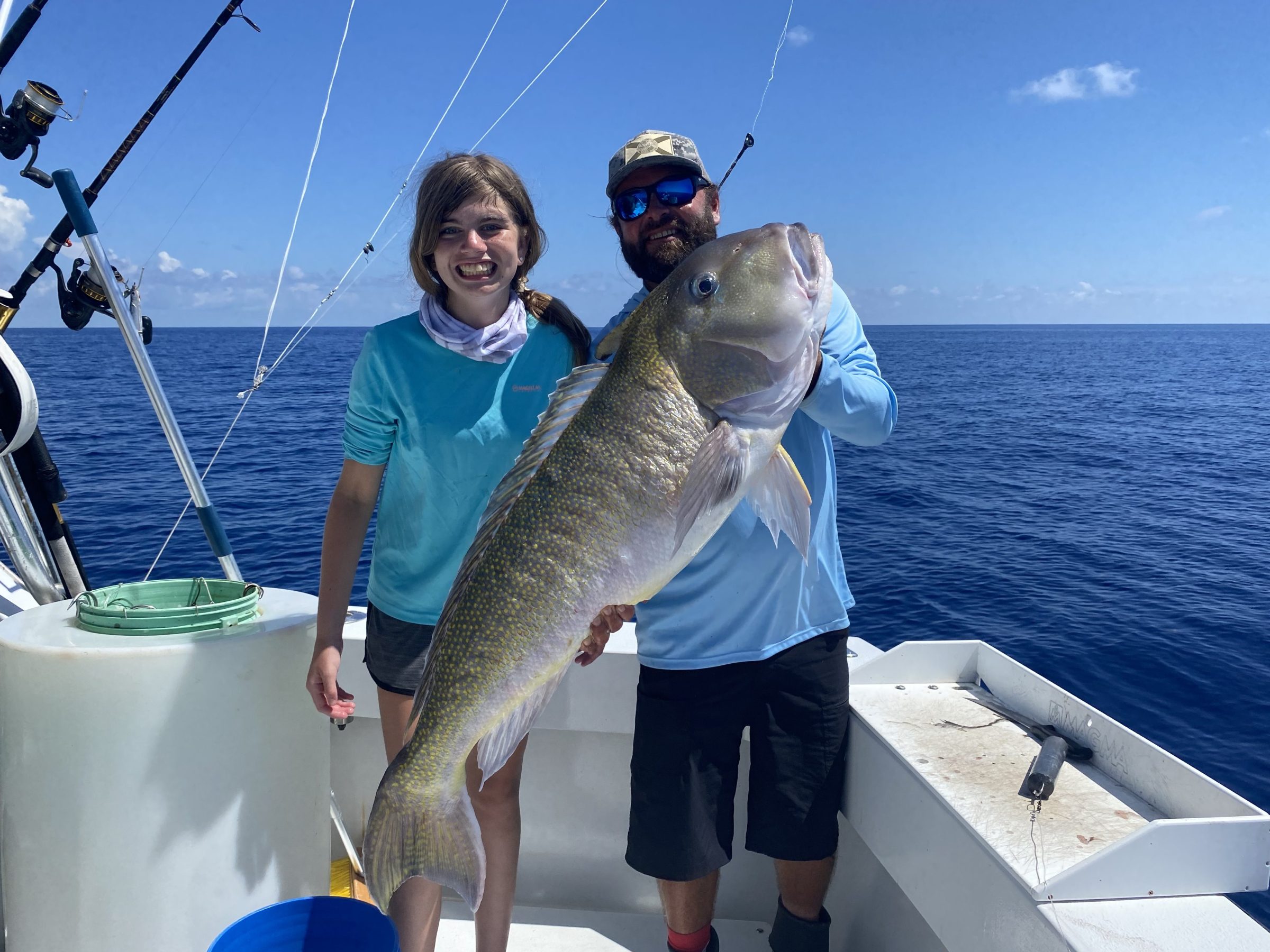 Two people on a boat holding a large fish with ocean in the background.