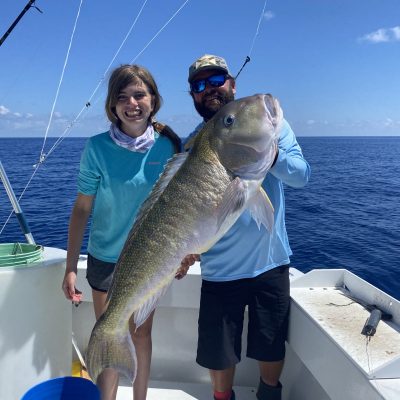 Two people on a boat holding a large fish with ocean in the background.