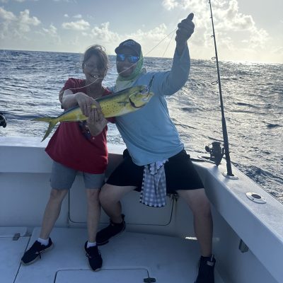 Two people on a boat holding a large fish, with the ocean and sky in the background.