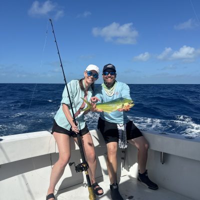 Two people on a boat, holding a fishing rod and a fish, with a blue ocean background.