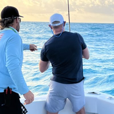Two people on a boat fishing in the ocean under a partly cloudy sky.