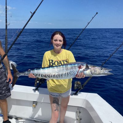 Person on boat holding large fish with ocean in background on a sunny day.