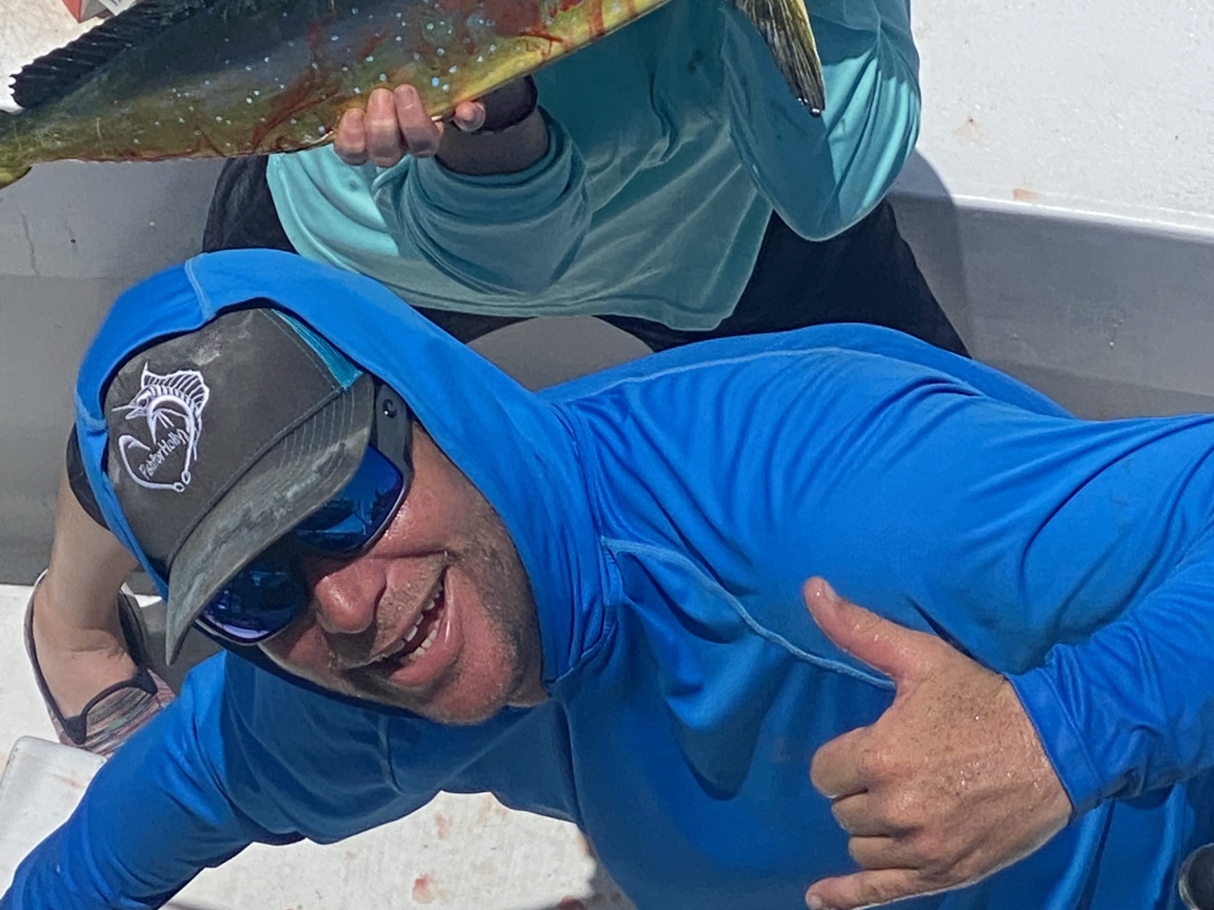 Two people on a boat showing off a large fish, one holding it and the other making a hand gesture.