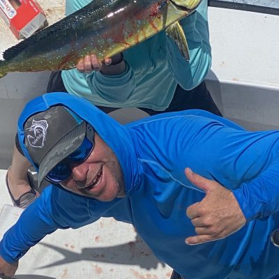 Two people on a boat showing off a large fish, one holding it and the other making a hand gesture.
