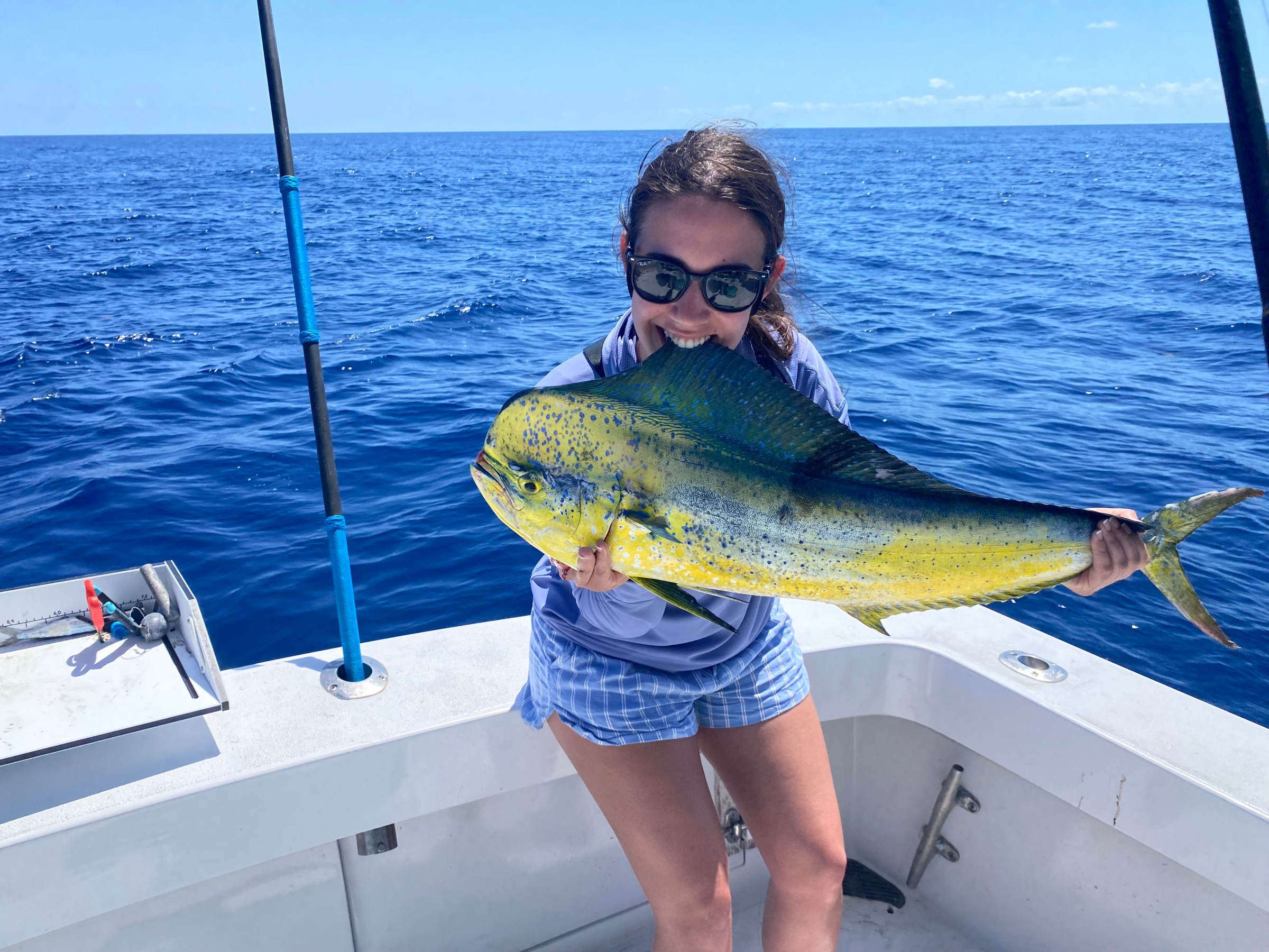 Person holding a large fish on a boat with ocean in the background.