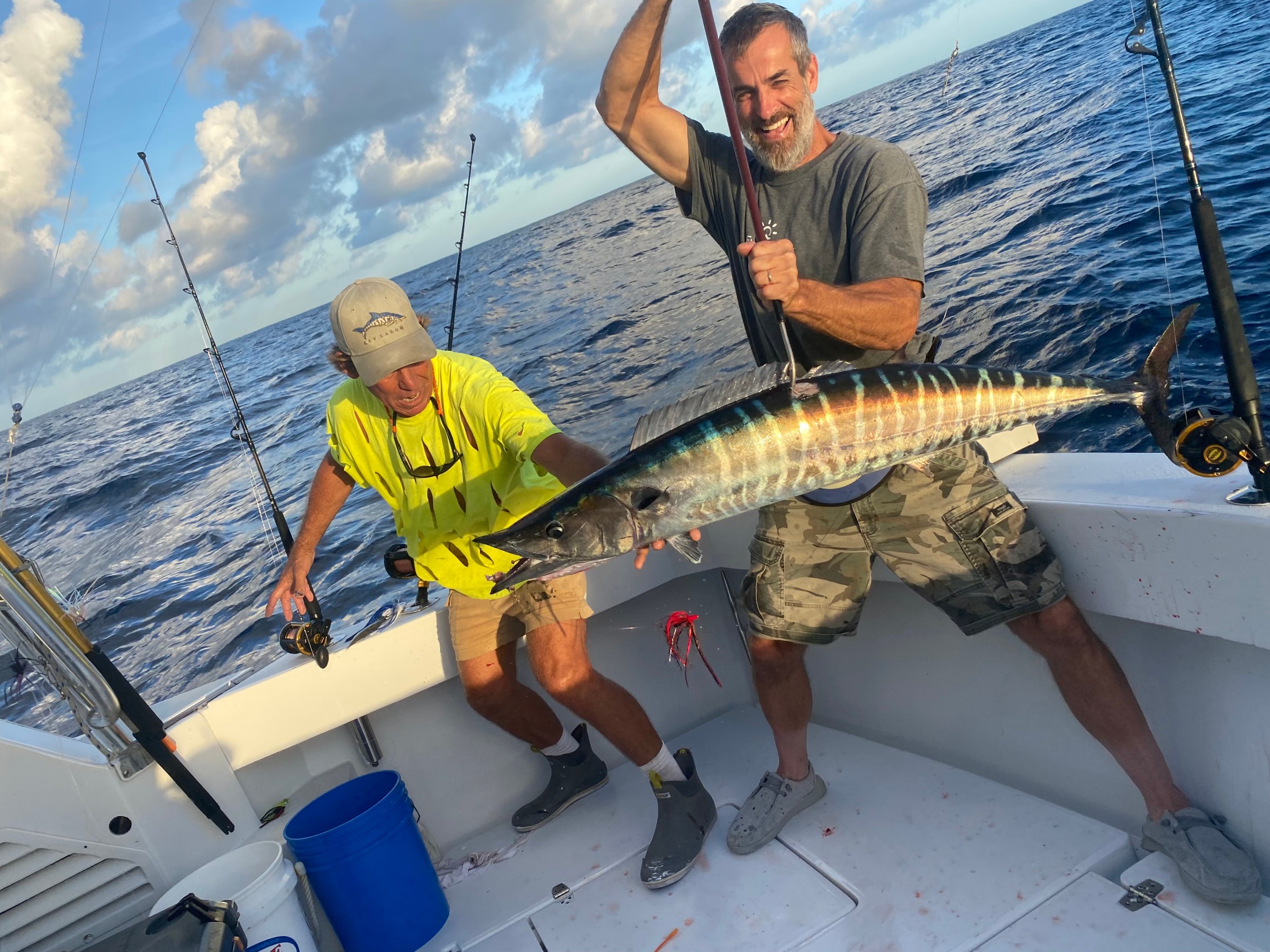 Two people on a boat holding a large fish with fishing rods in the background.