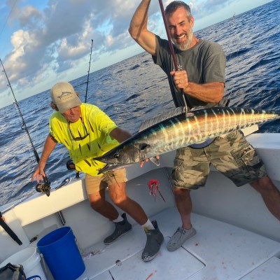 Two people on a boat holding a large fish with fishing rods in the background.