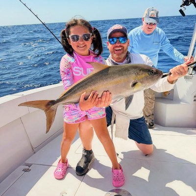 Smiling child and two adults holding a large fish on a boat at sea.