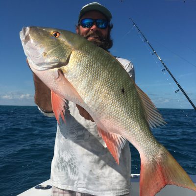 Man holding large fish on a boat with fishing rods and ocean in the background.