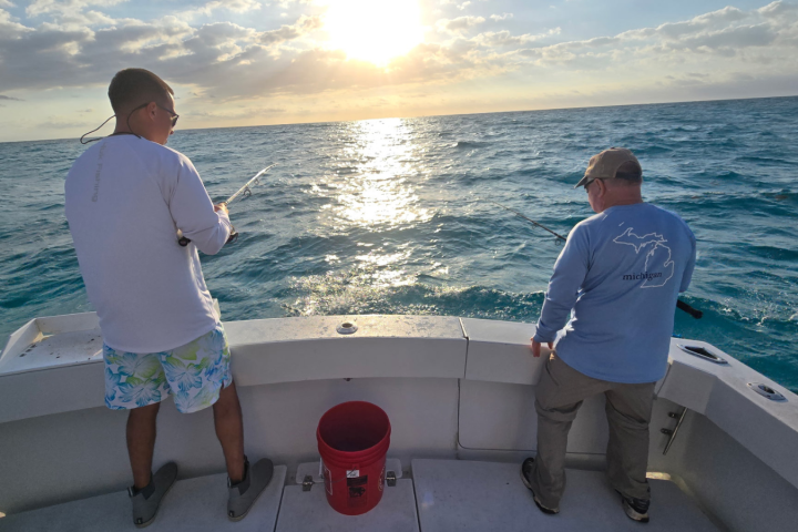 Two people fishing from a boat at sunset on the ocean.